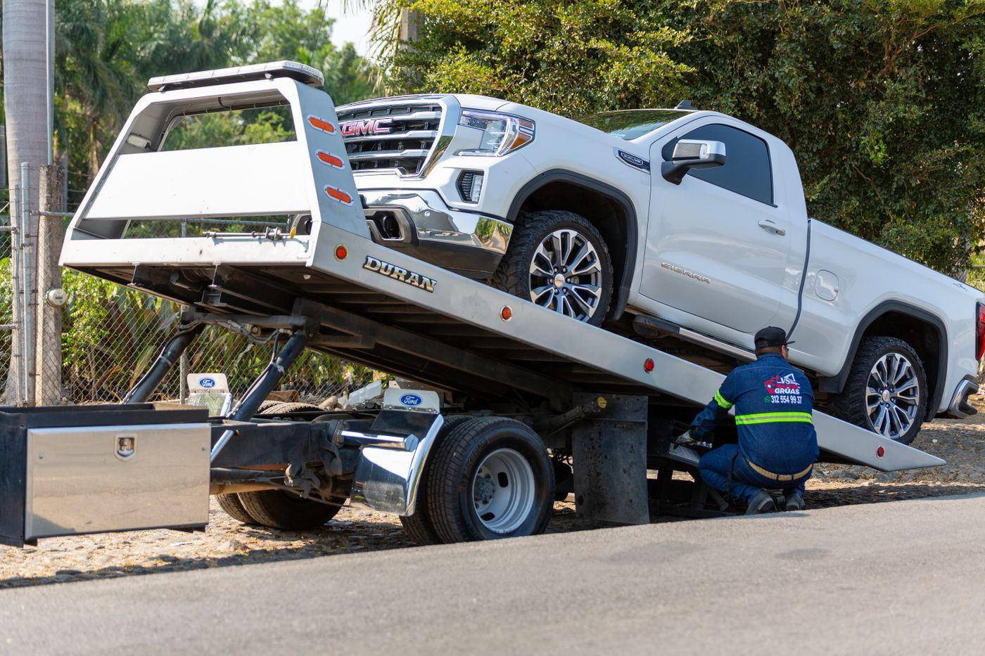 White pickup being loaded onto a tilted flatbed tow truck.