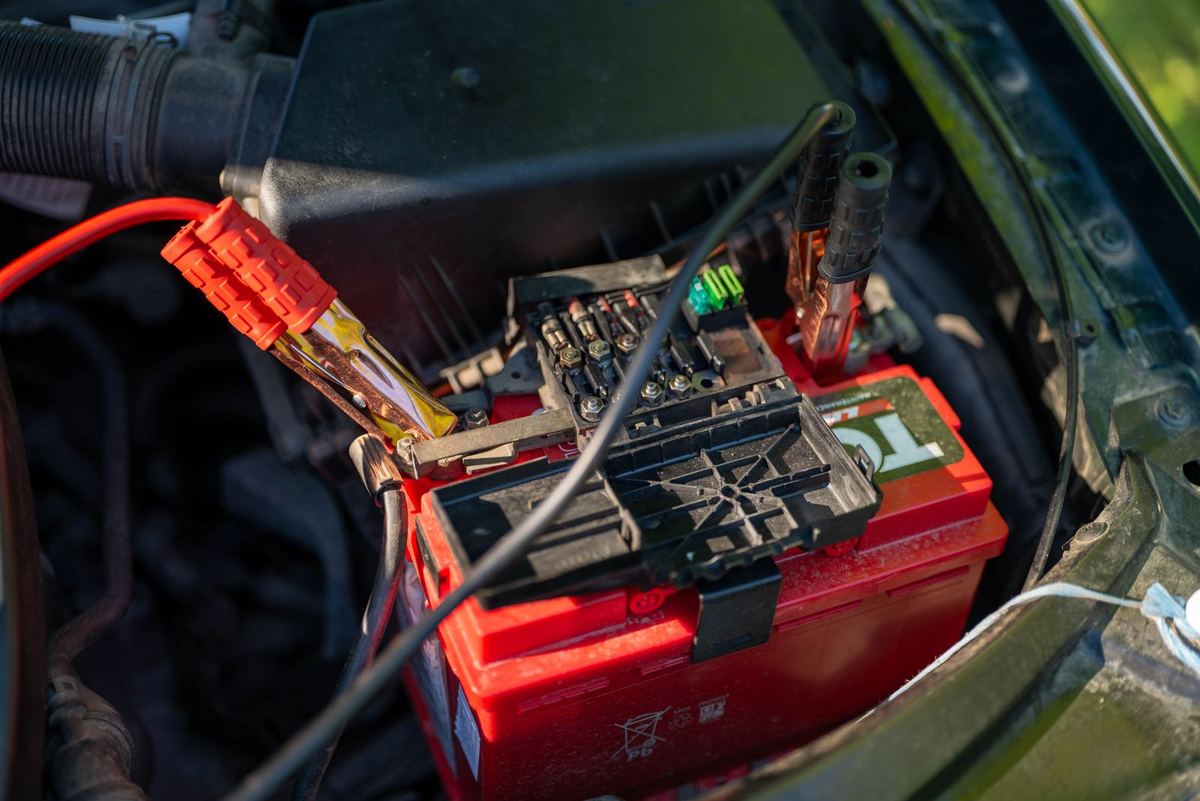 Close-up of jumper cables clamped to a car battery in an engine bay.